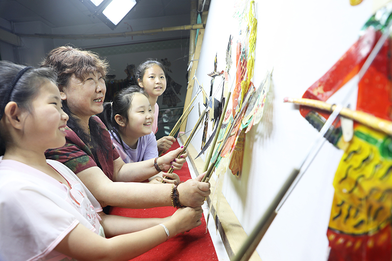 皮影藝人指導(dǎo)小朋友表演皮影戲。